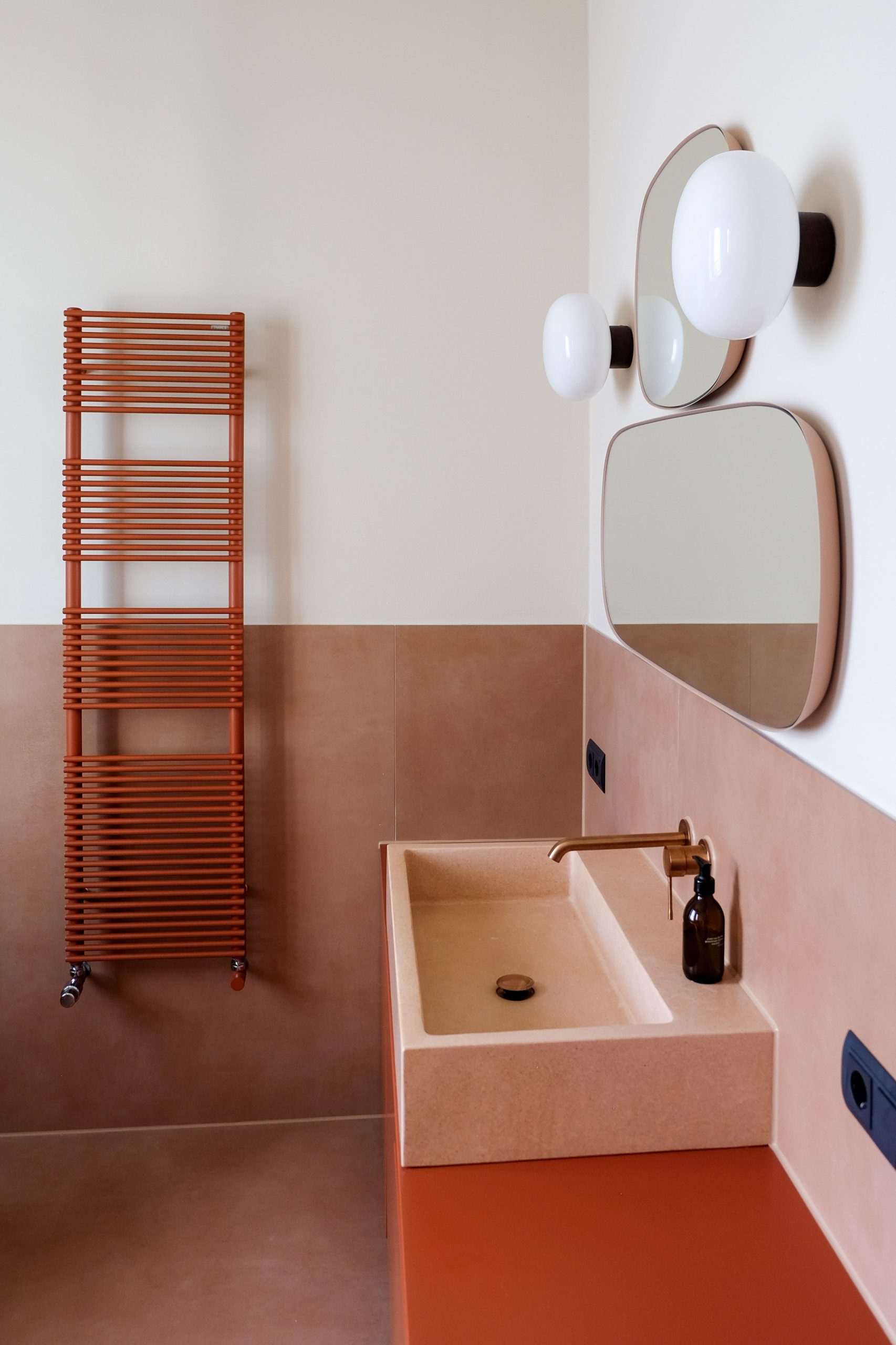 Badezimmer mit Waschbecken, Heizkörper und Armaturen in warmen Tönen auf maßgefertigten Möbeln in Rottönen. 